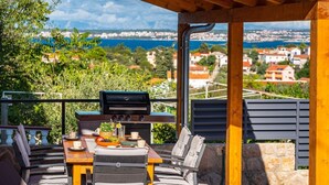 Un patio exterior con una parrilla, mesa de comedor, sillas y vistas a un pueblo costero.
