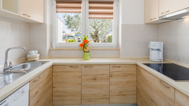 A kitchen with wooden cabinets, a built-in dishwasher, a window with blinds, and a coffee maker. - Family friendly, quiet location, garden with barbecue, near the beach (Poreč)