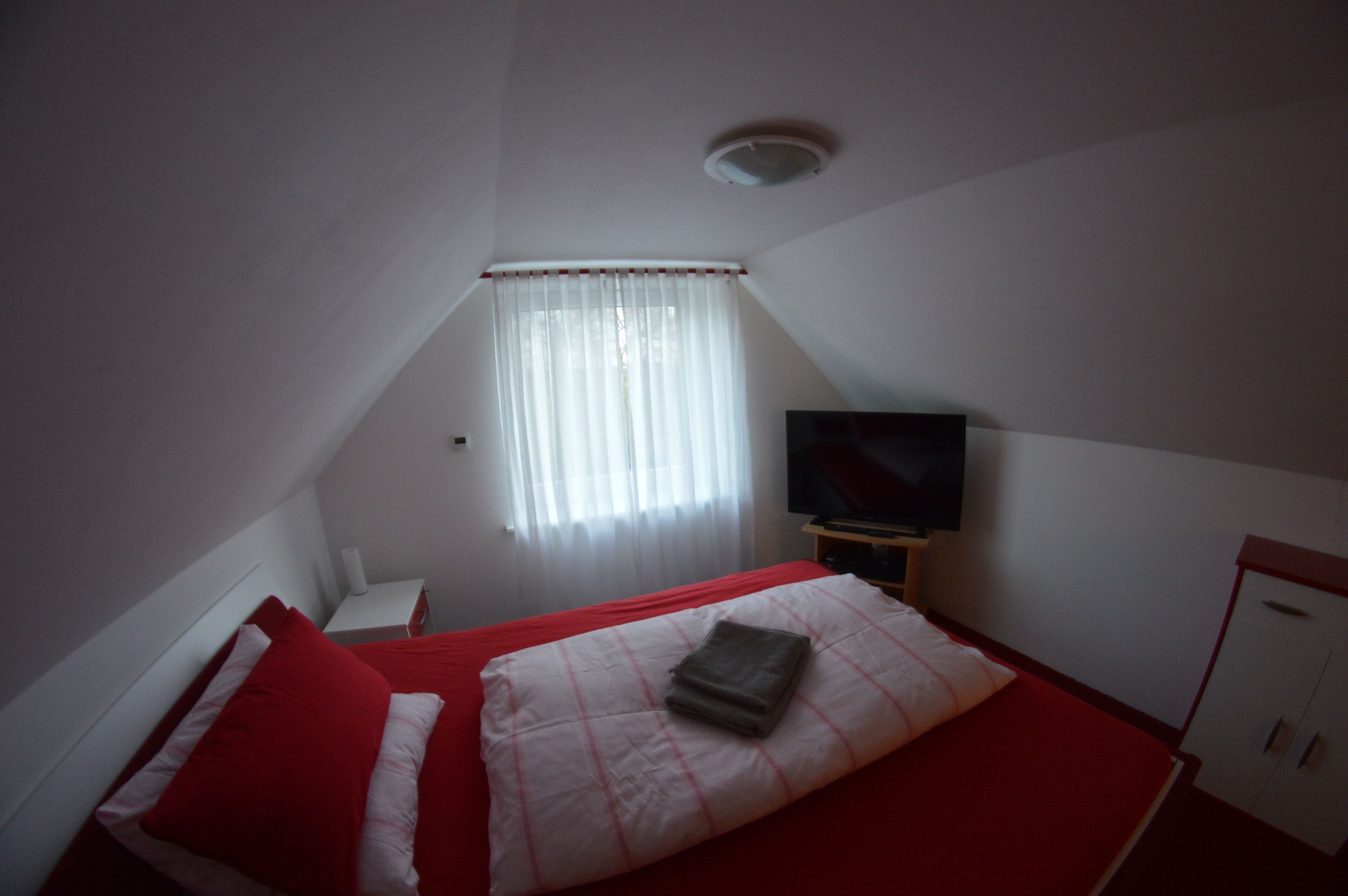A bedroom with a bed, a TV, a nightstand, and a window with curtains.
