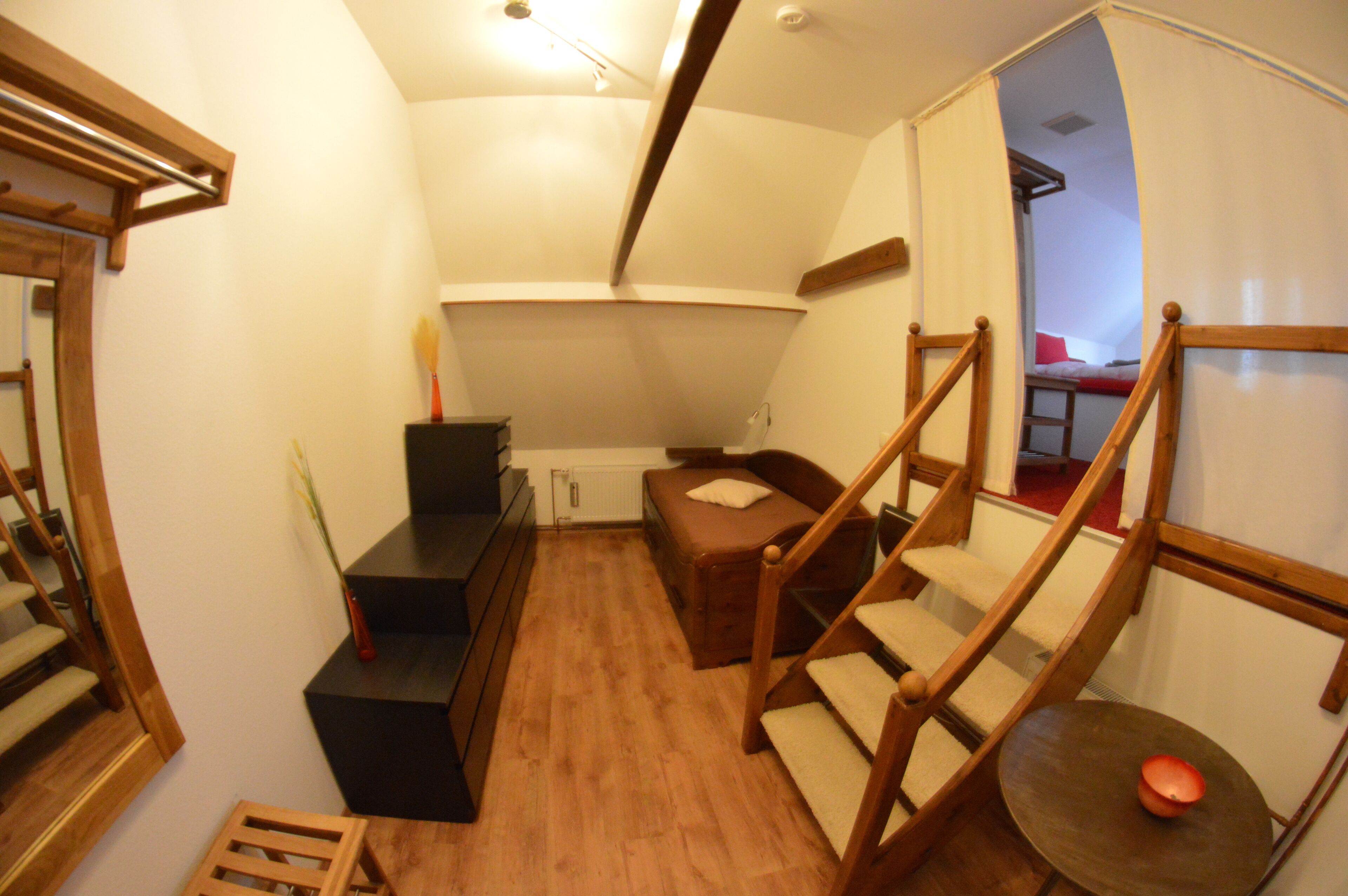 A compact room with a wooden staircase, a small bed, a desk, and a radiator.