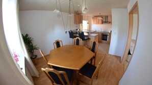 Een eetruimte met een houten tafel en stoelen, een potplant en hangende hanglampen.