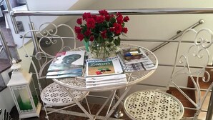 Une table à structure métallique, sur laquelle se trouvent un vase de roses rouges, des magazines et un petit récipient blanc.