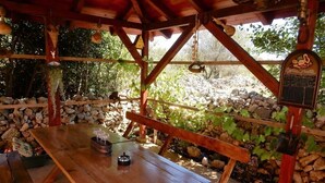 Une table en bois installée à l’extérieur, avec des bancs, entourée de murs en pierre et de verdure.