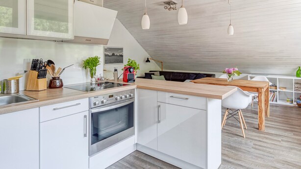 Une cuisine moderne avec des meubles blancs, un four encastré et un plan de travail en bois. On y trouve également un coin repas avec une table et des chaises blanches.