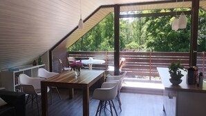 Un intérieur moderne comprenant un coin repas, des chaises blanches, une table en bois et une vue sur un jardin luxuriant, visible à travers de grandes fenêtres.