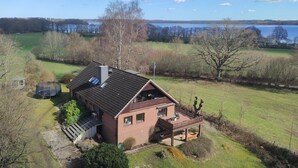 Une maison à deux étages avec une terrasse, un trampoline et une vue sur un lac.
