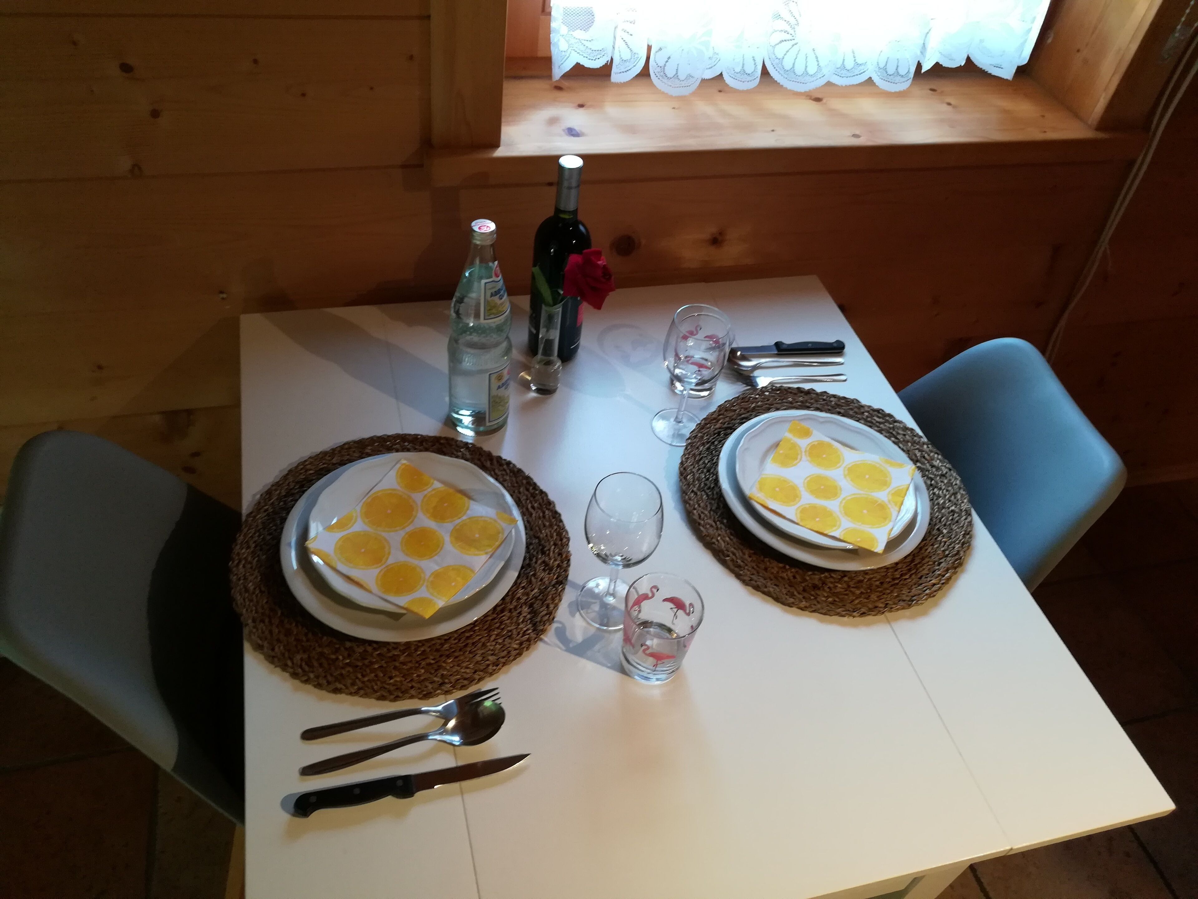 Ein Esstisch, gedeckt mit Tellern, Besteck, Gläsern und einer Flasche.