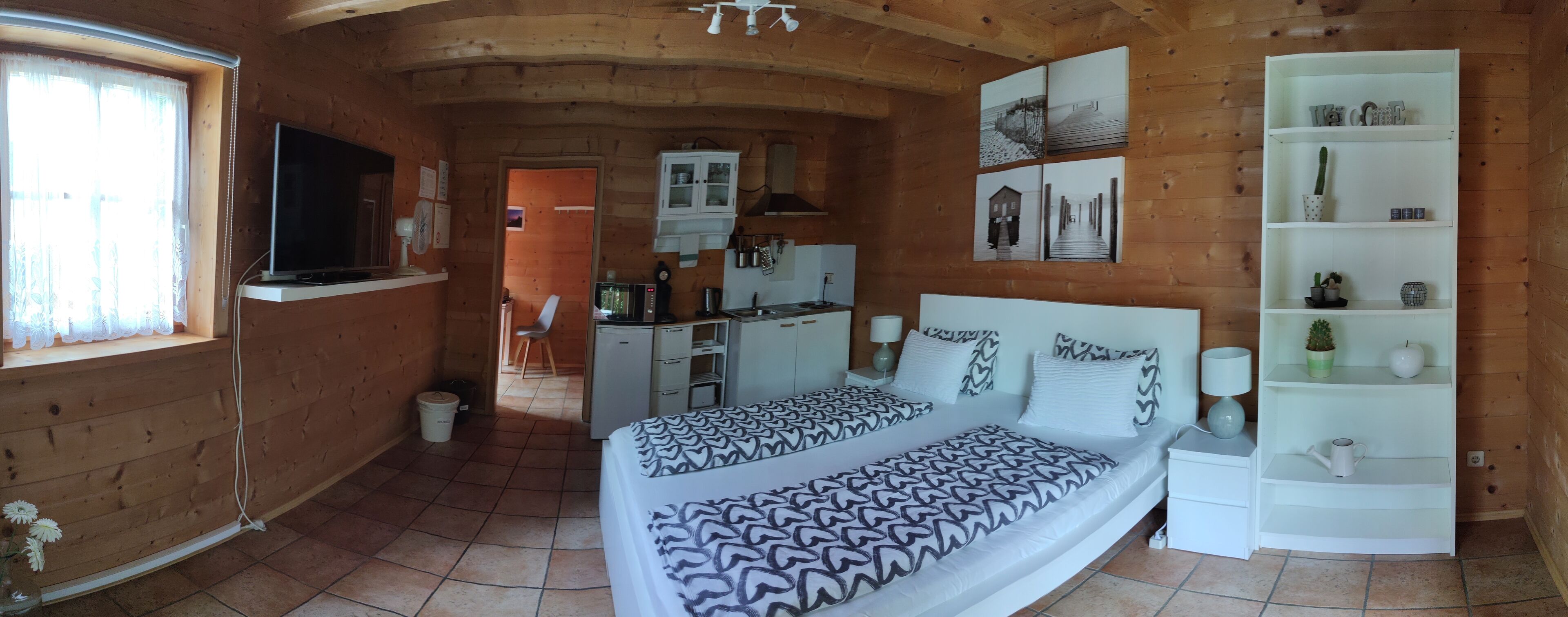 Ein gemütliches Zimmer mit Bett, Fernseher, Schreibtisch und einer Küchenzeile.