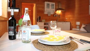 Un intérieur en bois avec une table à manger dressée pour deux personnes, agrémentée d’assiettes décorées de tranches de citron, d’une bouteille de vin blanc et d’une bouteille de vin rouge.