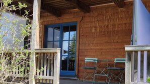 Une cabane en bois avec une véranda, une porte bleue et deux chaises pliantes.