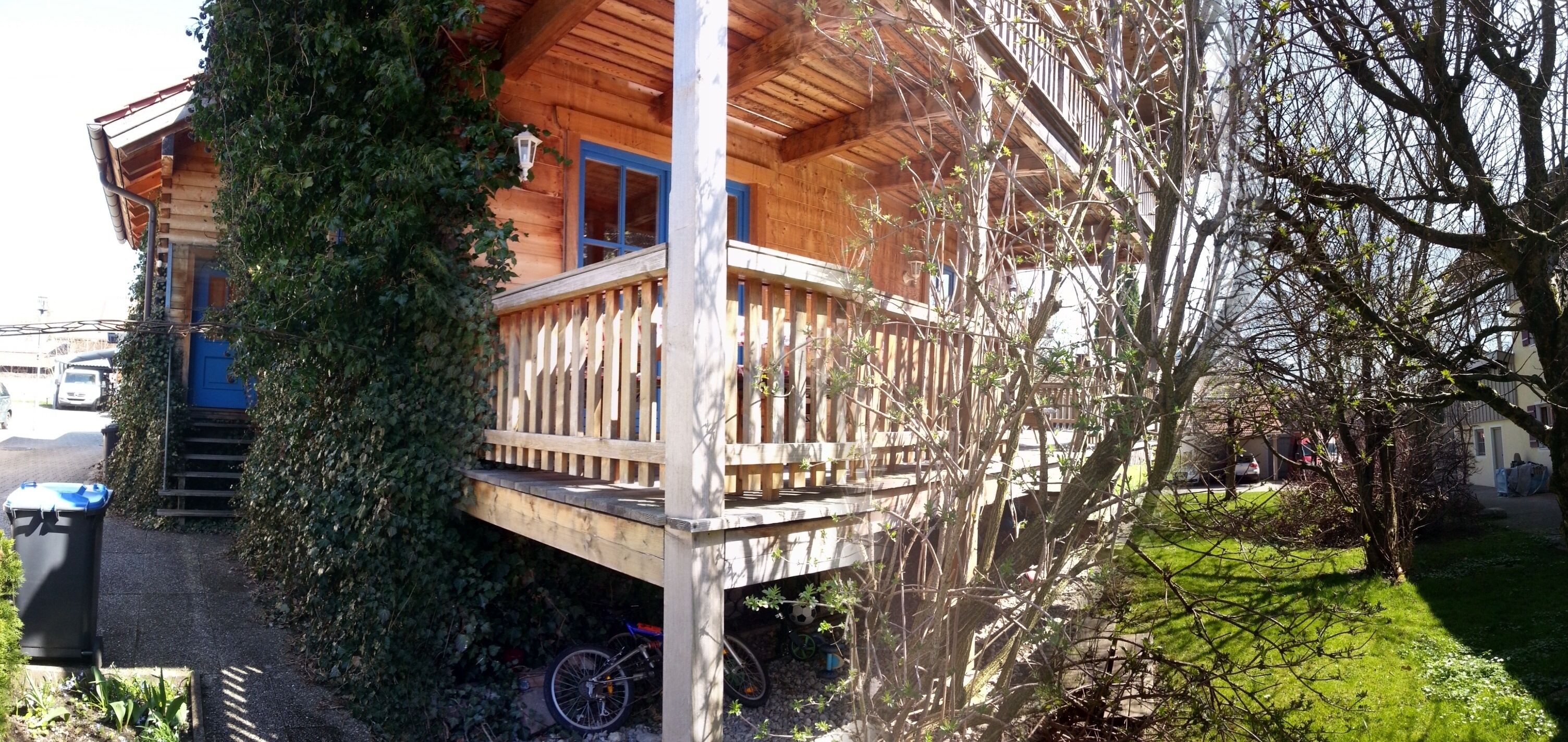 Una cabaña de madera con balcón, rodeada de follaje y una bicicleta.