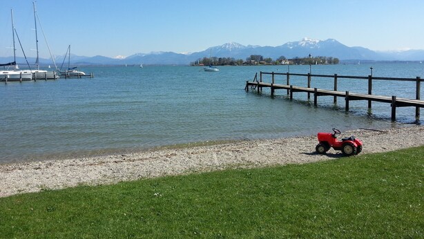 Une scène au bord d’un lac, avec un quai, des bateaux et une petite voiture rouge sur la rive.