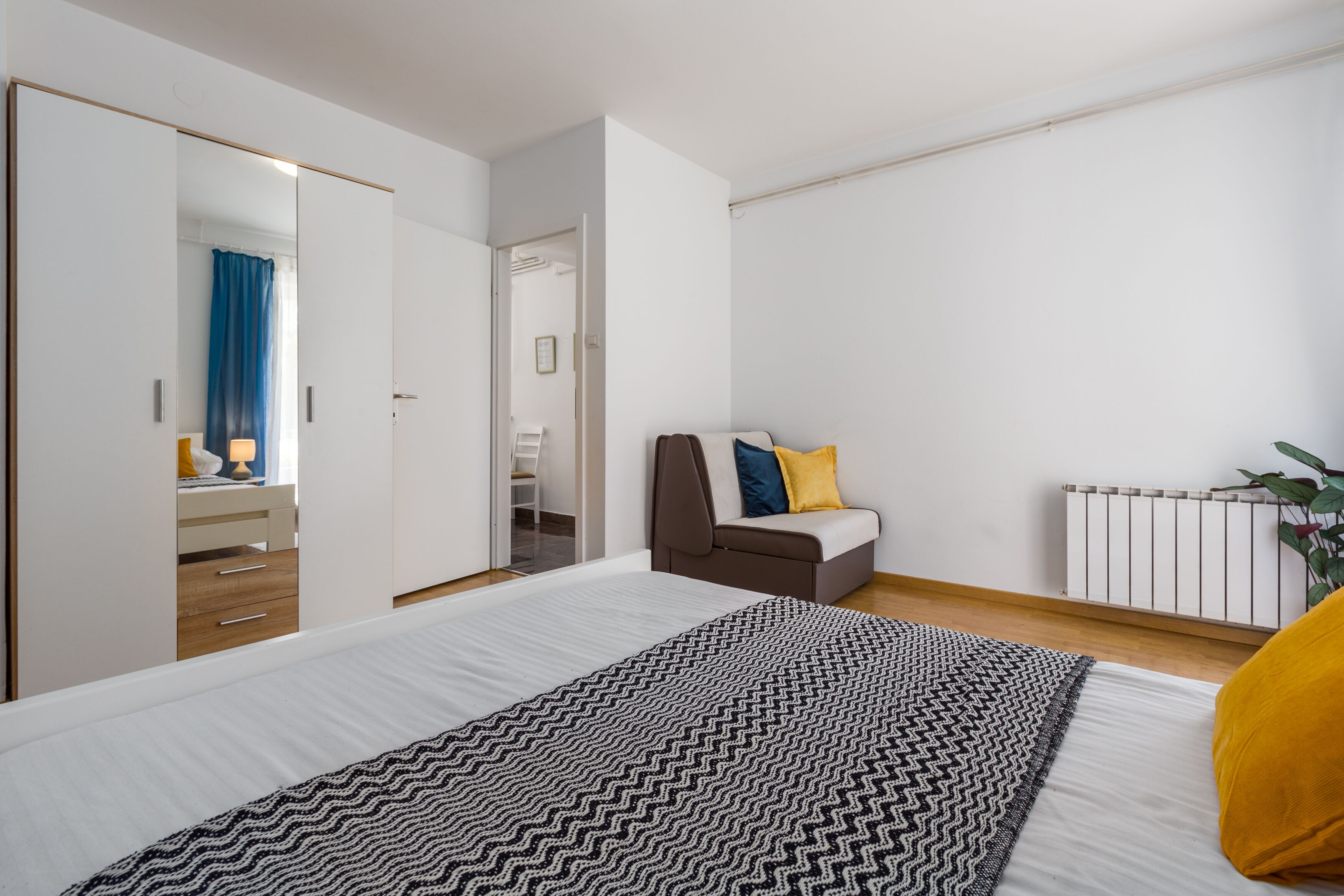 A bedroom with a bed, a sofa, a mirror, a radiator, and a plant.