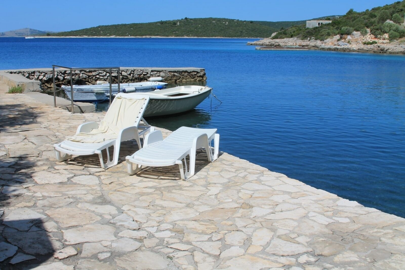 A stone-paved dock with white lounge chairs and a boat.