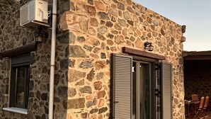 Un edificio de piedra con una ventana, una puerta y un pequeño espacio al aire libre para sentarse.