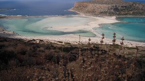 Un paisaje costero con playa, aguas claras y una colina rocosa al fondo.