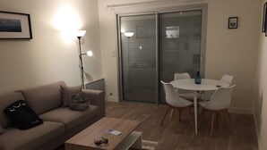 A living room with a sofa, coffee table, and a dining table with chairs. There is a sliding glass door and a framed picture on the wall. - Apartment in a Richmond hill residence (Tours)