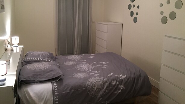A bedroom with a bed, a dresser, a nightstand, a lamp, and a window with curtains. - Apartment in a Richmond hill residence (Tours)