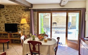 Un coin repas avec un mur en pierre, un téléviseur et une table agrémentée d’un panier de fruits et de fleurs.