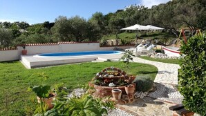 Ein Garten mit Swimmingpool, einem Feuerkorb aus Ziegelsteinen und einem Gartenbereich mit Blumentöpfen.
