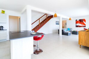 A modern kitchen with a central island, a staircase, and a living area with a sofa and coffee table. - Bois Lélé (Le Vauclin)
