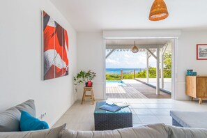 A modern living room with a large painting, a view to the outside, a wooden bench, and a glass coffee table. - Bois Lélé (Le Vauclin)