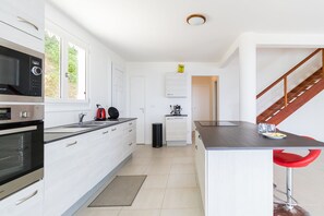 A modern kitchen with built-in appliances, a dining area with a table and chairs, and a staircase leading to another level. - Bois Lélé (Le Vauclin)