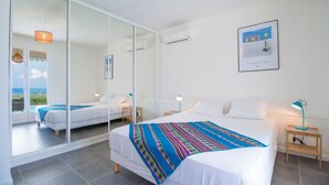 A modern hotel room with a large bed, a mirror, a framed artwork, and a view of the sea.