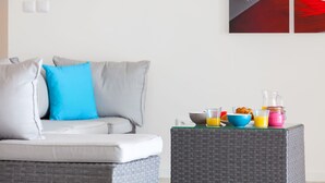 A modern living room with a grey sofa, a blue pillow, and a wicker coffee table with breakfast items.