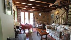 A cozy living room with a wooden staircase, stone walls, a patterned sofa, and a dining area with a red tablecloth. - Charming Individual cottage" La Petite Grange" for maximum 4 people   (Puybrun)