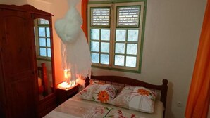 A bedroom with a wooden bed, a nightstand with a lamp, and a window with shutters.