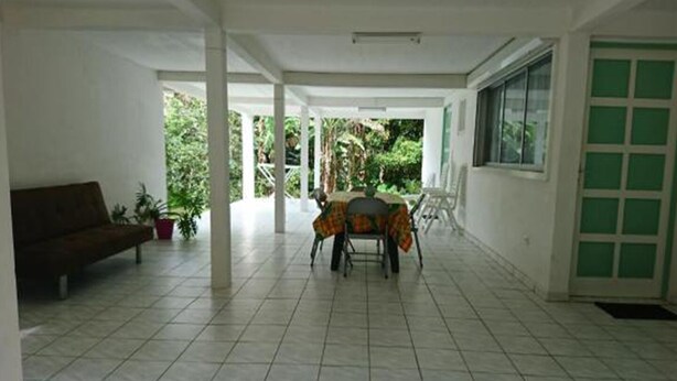 A spacious indoor area with a tiled floor, a sofa, a table with chairs, and a window with green-tinted glass.