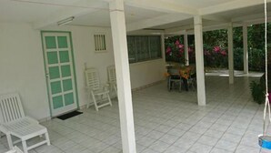 A covered outdoor area with tiled flooring, a green door, white chairs, and a table with chairs.