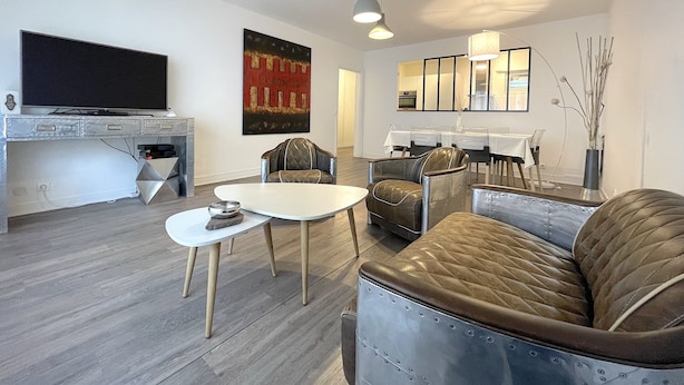 A modern living room with a flat-screen TV, a dining area with a table and chairs, and a seating area with a sofa and armchairs. - Apartment in Deauville center with PARKING and BEACH CABIN (Deauville)