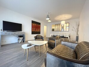 A modern living room with a flat-screen TV, a dining area with a table and chairs, and a seating area with a sofa and armchairs. - Apartment in Deauville center with PARKING and BEACH CABIN (Deauville)
