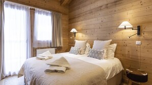 Ein Schlafzimmer mit Holzwänden, einem großen Bett, zwei Wandleuchten und einem Fenster mit durchsichtigen Vorhängen.