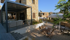 A modern stone building with a covered outdoor seating area, a gravel patio, and a view of the surrounding neighborhood. - Sea-view villa, 1.5 km from beaches, private heated pool (optional). (KONTOMARI)