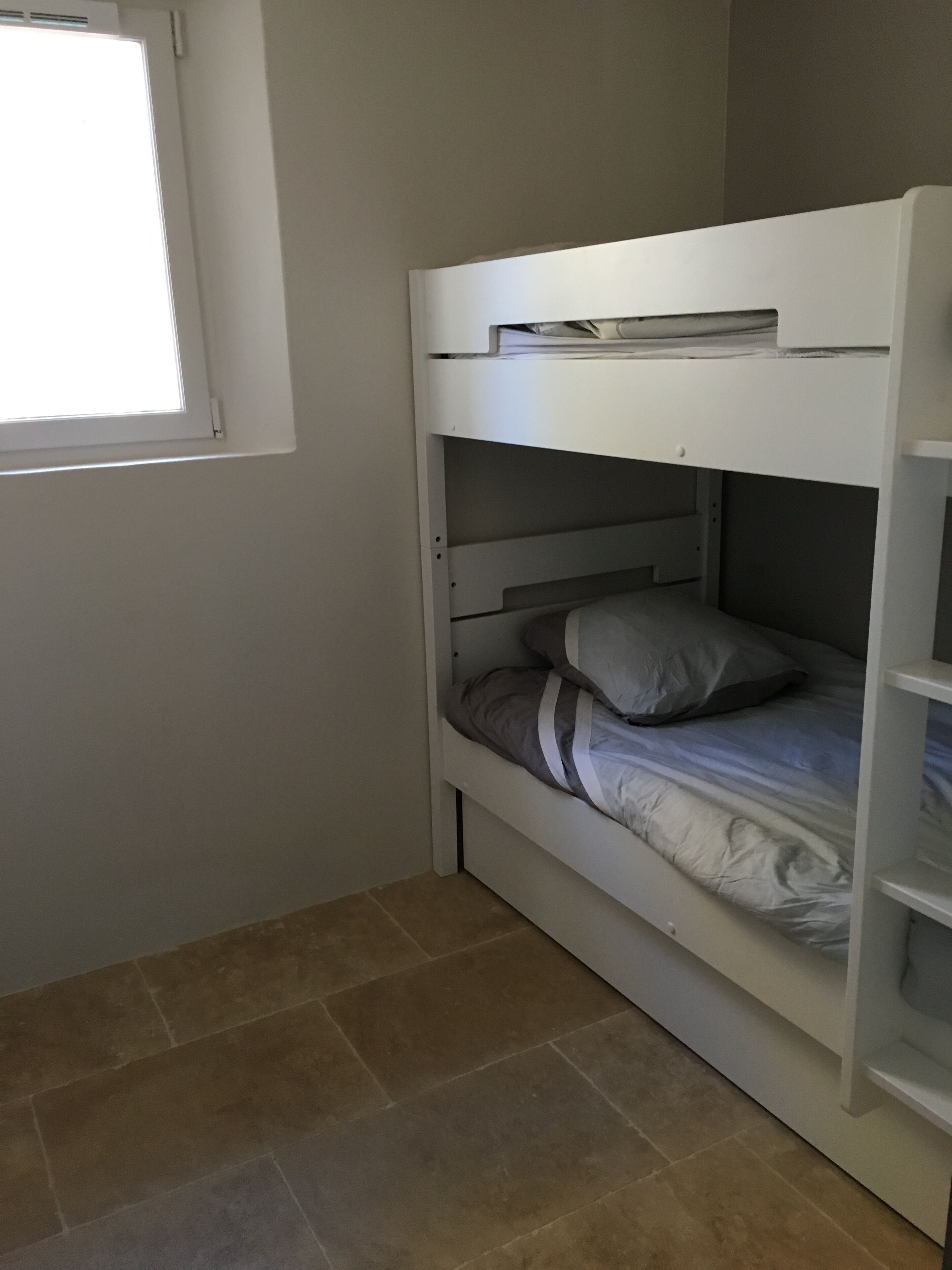 A bunk bed with a desk and shelving unit, a window, and tiled flooring.