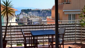 A balcony with a table and chairs, overlooking a cityscape with buildings and a cliff. - AMAZING APARTMENT LOFT NEAR THE BEACHES (Cap-D'ail)