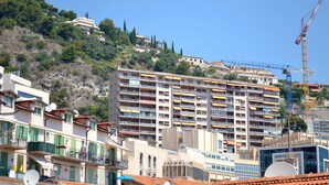 A multi-story residential building with balconies, a construction crane, and a hillside with trees. - AMAZING APARTMENT LOFT NEAR THE BEACHES (Cap-D'ail)