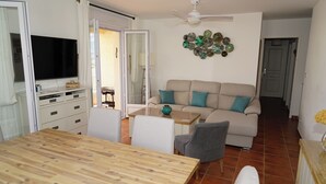 En stue med et træspisebord, en beige sofa med teal farvede puder, et fjernsyn og et kunstværk på væggen.