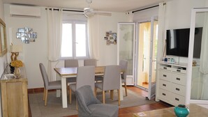 A dining area with a table and chairs, a television on a stand, and a cabinet with drawers. - Stunning 82m² air-conditioned 4-bedroom apartment in a villa in Calvi (Calvi)