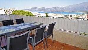 An outdoor terrace with a table and chairs, overlooking a coastal area with buildings and mountains. - Stunning 82m² air-conditioned 4-bedroom apartment in a villa in Calvi (Calvi)