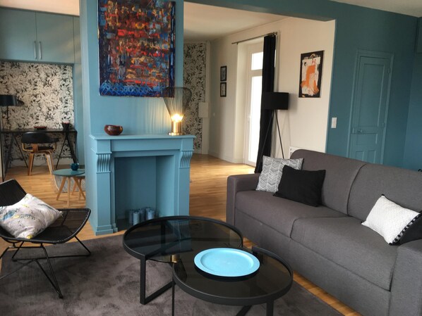 A living room with a blue fireplace, a grey sofa, a glass coffee table, and a dining area with a table and chairs.
