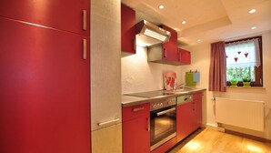 Une cuisine avec des meubles de couleur rouge, des appareils électroménagers en acier inoxydable et une fenêtre avec des rideaux.