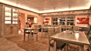 Un vaste espace dédié à la salle à manger, avec des tables et des chaises en bois, un grand meuble avec des portes en verre, et une vue sur la ville grâce à de grandes fenêtres.