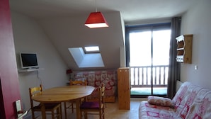 Une pièce chaleureuse avec une table à manger en bois, des chaises, un canapé, un téléviseur et un balcon doté d’une balustrade.