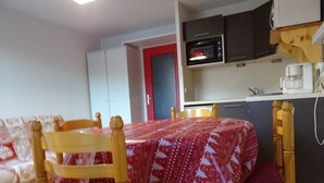 Une cuisine compacte équipée d’un four à micro-ondes, d’une machine à café et de placards. On y trouve une table à manger avec des chaises et une nappe rouge.