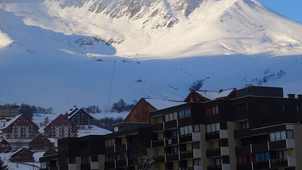 Une montagne avec un télésiège et des bâtiments enneigés au premier plan.