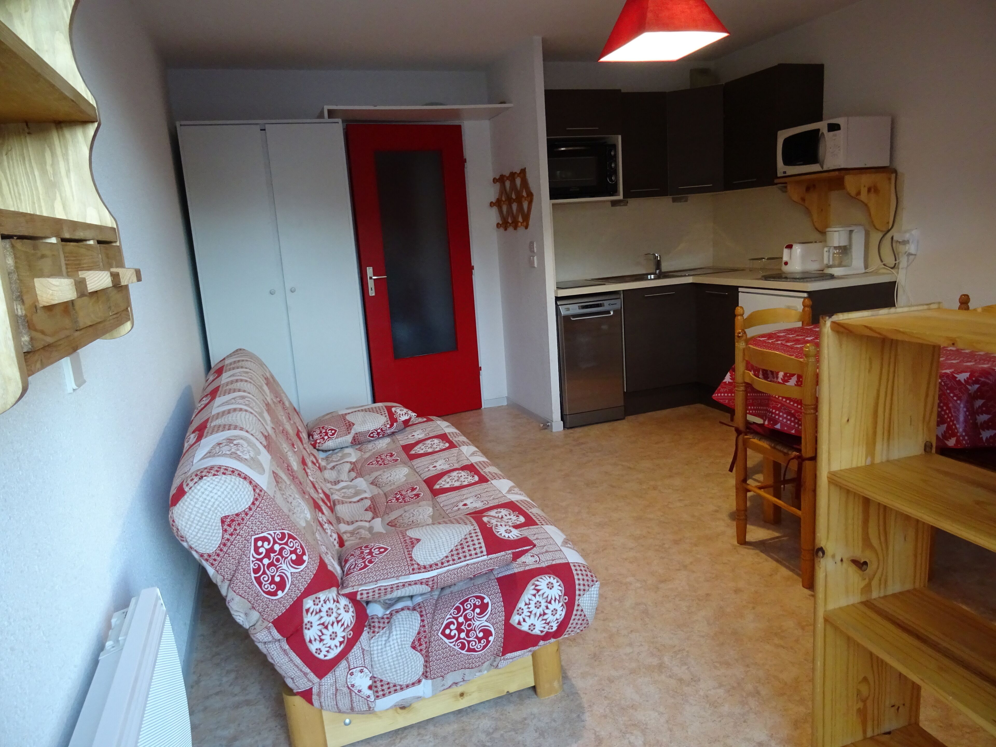 Un espacio habitable compacto con kitchenette, un sofá, una mesa de comedor y una puerta roja.